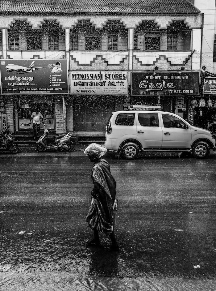 A pedestrian walks along a rainy street in Karaikudi, India, capturing local life.